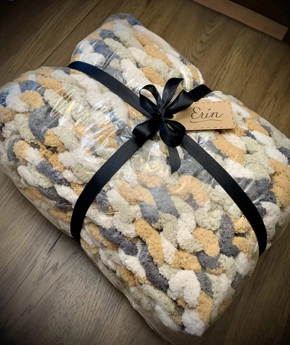 A knit blanket folded, wrapped and tied with a black ribbon and a gift tag