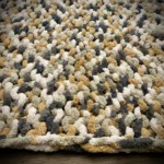 A chunky knit blanket in gray, gold and white, laid flat