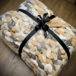 A knit blanket folded, wrapped and tied with a black ribbon and a gift tag