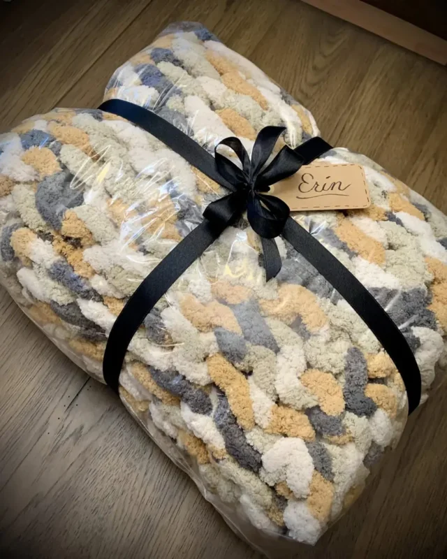A knit blanket folded, wrapped and tied with a black ribbon and a gift tag